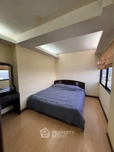 Cozy bedroom with large window offering city views and natural light, featuring a comfortable bed and wooden flooring.