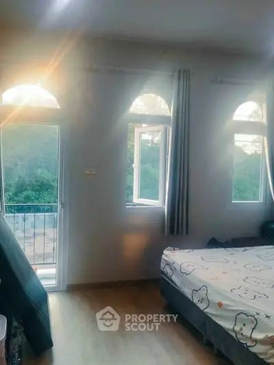 Cozy bedroom with large windows and balcony access, offering serene views of lush greenery.