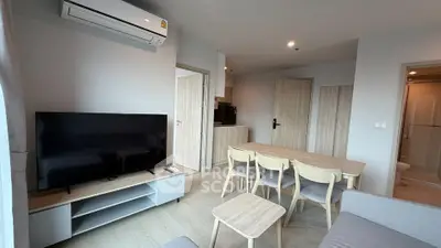 Modern living room with sleek furniture and open layout, featuring a large TV and air conditioning.