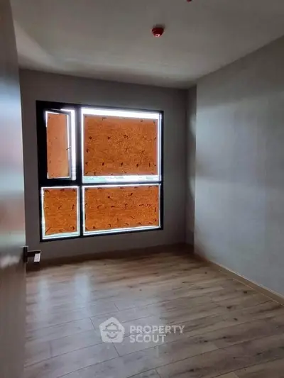 Spacious empty room with large window and wooden flooring, ideal for customization.