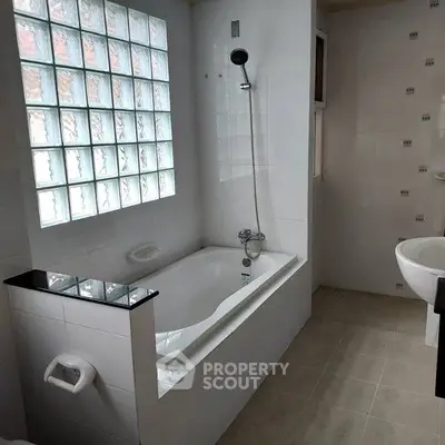 Modern bathroom with glass block window and sleek bathtub design.
