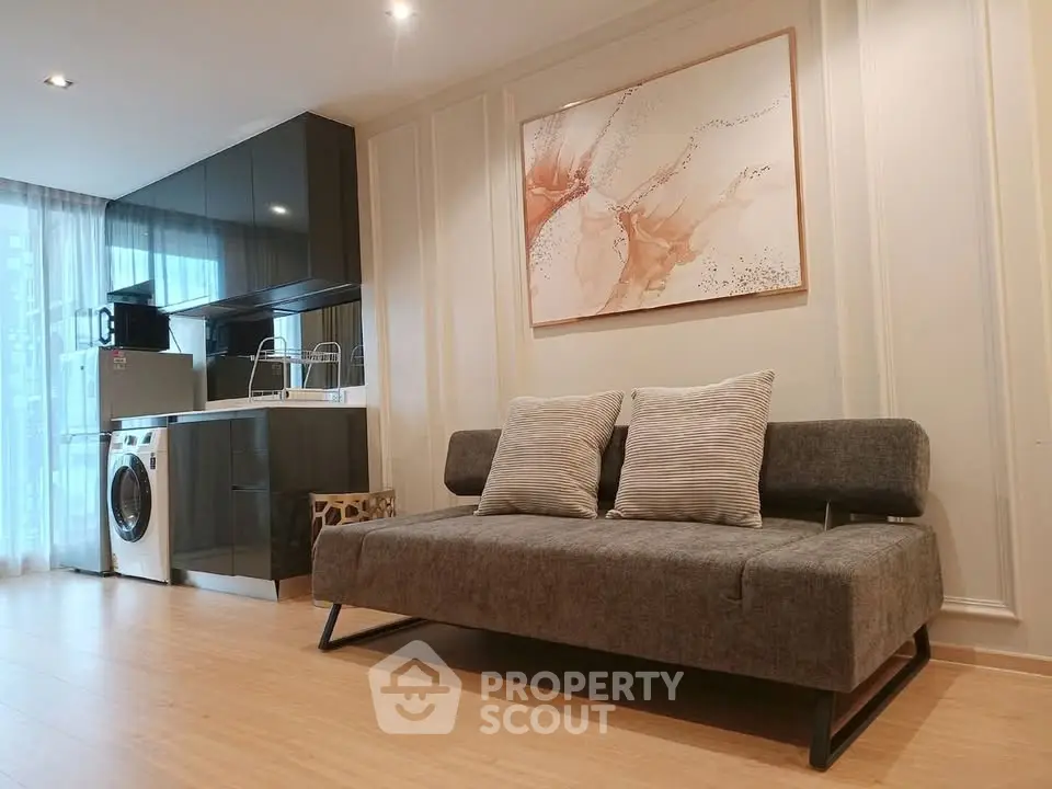Modern living room with sleek kitchen and washing machine, featuring stylish decor and natural light.