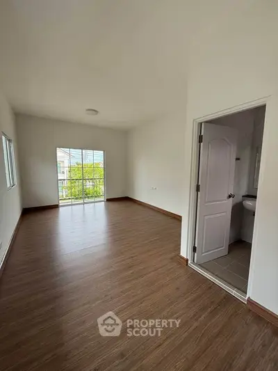 Spacious empty room with wooden flooring and balcony access, ideal for customization.