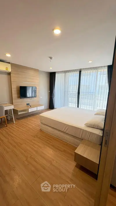 Modern bedroom with wooden flooring, large window, and wall-mounted TV in a stylish apartment.