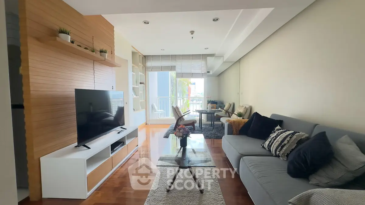 Spacious modern living room with stylish decor and large TV, leading to a bright balcony with outdoor seating.