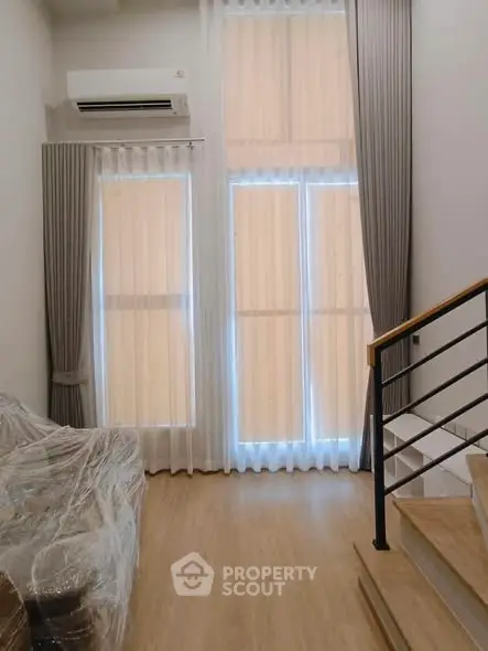 Modern living room with high ceilings and large windows, featuring elegant curtains and a staircase.