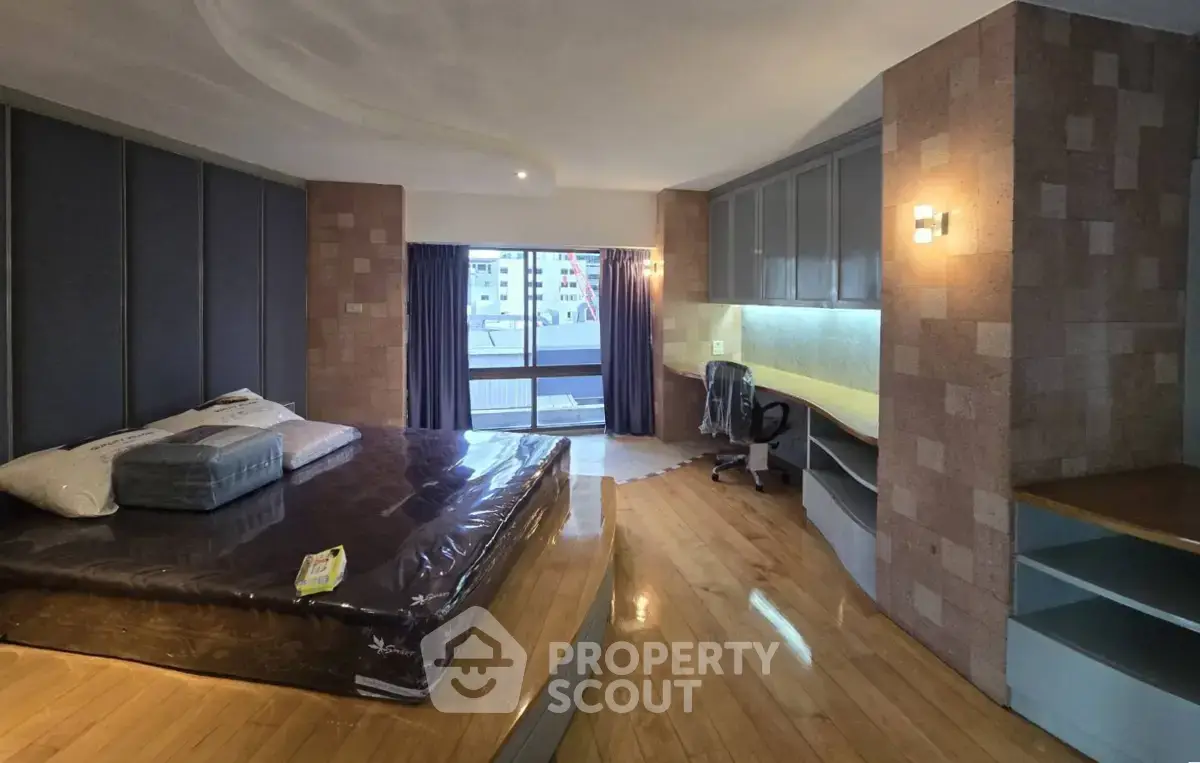 Spacious bedroom with modern design and built-in study area, featuring wooden flooring and large windows.