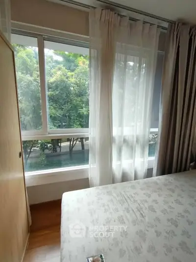 Cozy bedroom with large window offering lush green view