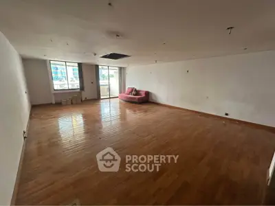 Spacious unfurnished room with wooden flooring and large window, ideal for customization.