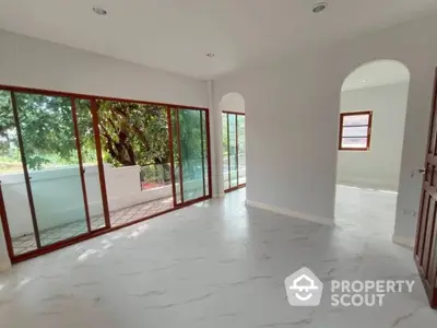 Spacious and bright living area with large sliding glass doors opening to a serene outdoor view, featuring elegant marble flooring and archway design.