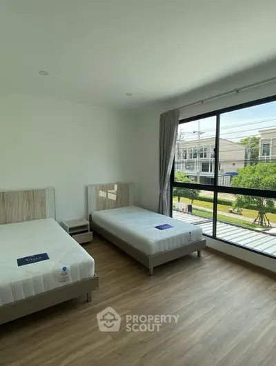 Spacious bedroom with twin beds and large window offering a serene view of the neighborhood.