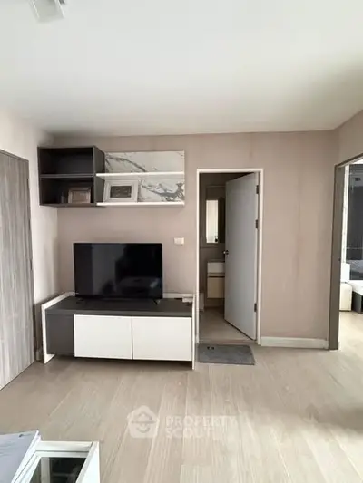Modern living room with sleek TV stand and open doorway to bathroom, featuring light wood flooring.