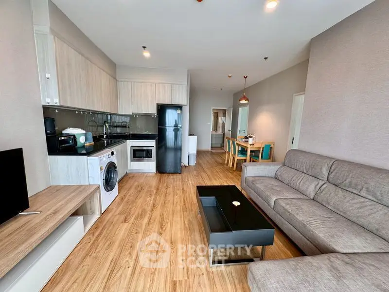 Modern open-layout living room with kitchen, featuring sleek appliances and stylish furniture.