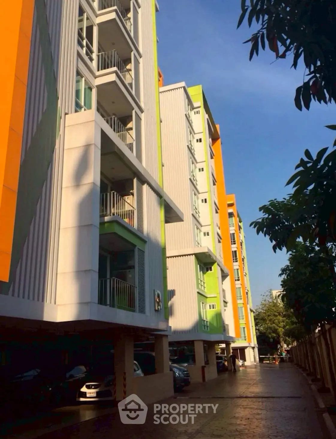 Modern apartment building with vibrant colors and shaded parking area.