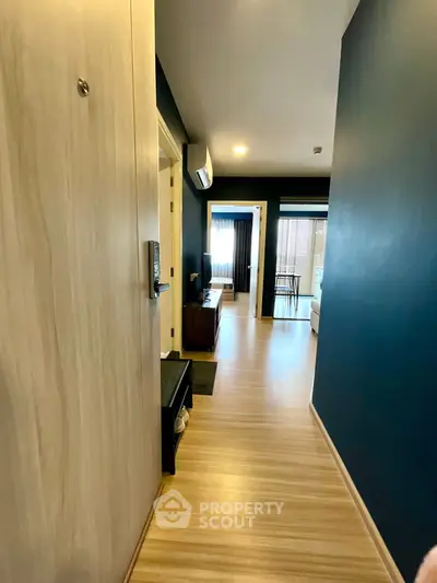 Modern apartment hallway with wooden flooring leading to a bright living area and balcony.