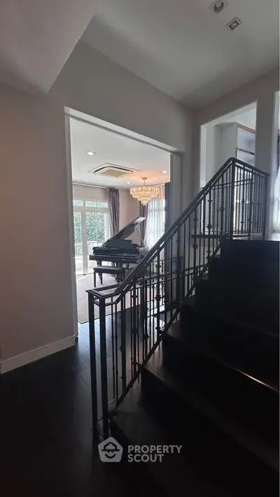 Elegant staircase leading to a grand piano room with chandelier and large windows.