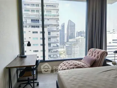 Modern bedroom with city view, featuring a cozy chaise lounge and work desk by the window.