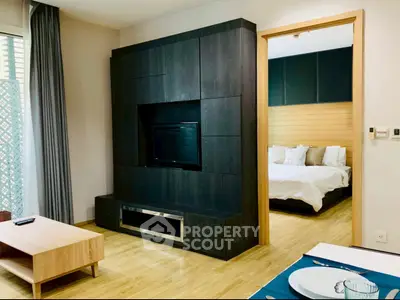 Modern living room with stylish dark wood entertainment center and view into cozy bedroom.