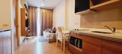 Modern open-layout living room with kitchen, featuring wooden flooring and elegant curtains.