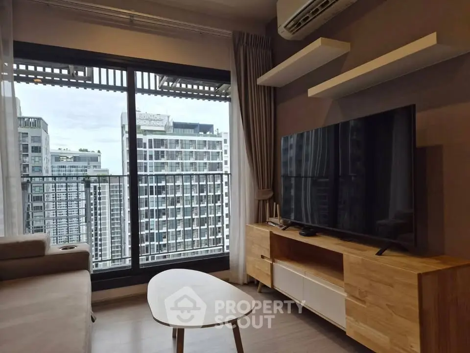 Modern living room with large TV and city view from balcony in high-rise apartment.