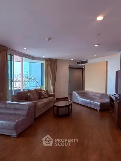 Spacious living room with large windows and modern furniture in a high-rise apartment.