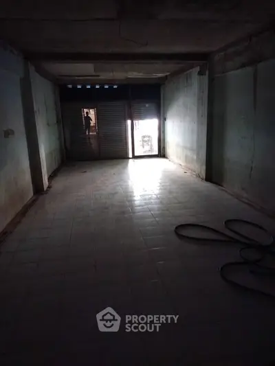 Spacious empty room with tiled floor and large window, ideal for renovation or storage.