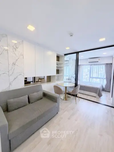 Modern studio apartment with open layout, featuring a cozy living area and stylish bedroom separated by glass partition.
