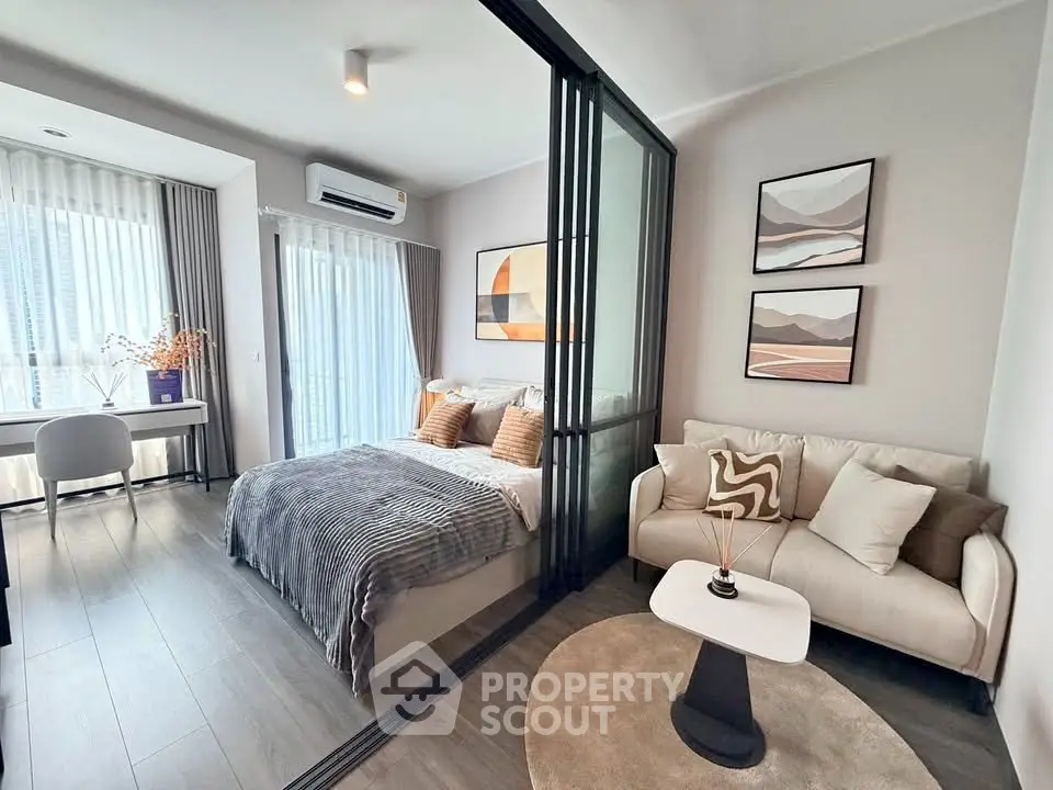 Modern bedroom with glass partition, cozy seating area, and stylish decor in a bright apartment.