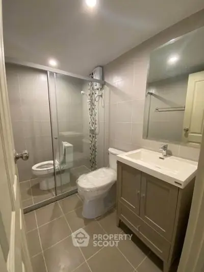 Modern bathroom with glass shower and sleek vanity in contemporary apartment.