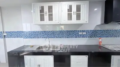 Modern kitchen with sleek black countertop and white cabinets, featuring a stylish blue mosaic backsplash.