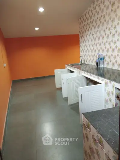 Spacious kitchen with vibrant orange walls and ample storage cabinets.