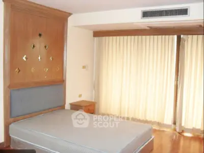 Spacious bedroom with large window and elegant wooden accents.