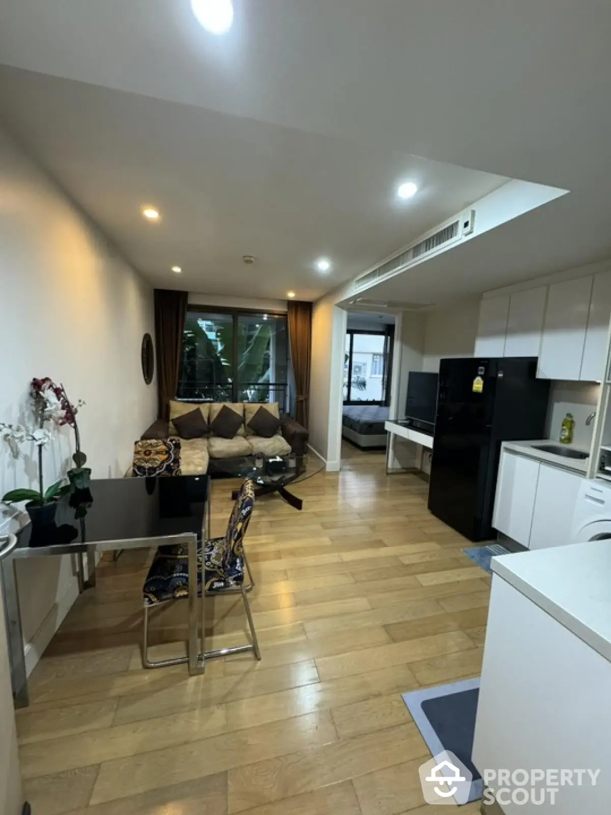 Modern open-plan living room with kitchen and dining area, featuring sleek furniture and wooden flooring.