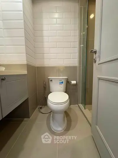 Modern bathroom with sleek tiles and compact design, featuring a toilet and shower area.