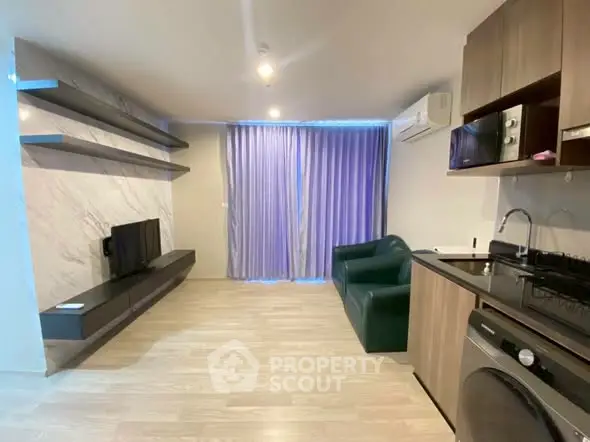 Modern living room with sleek shelves, TV, and compact kitchen featuring washing machine and microwave.