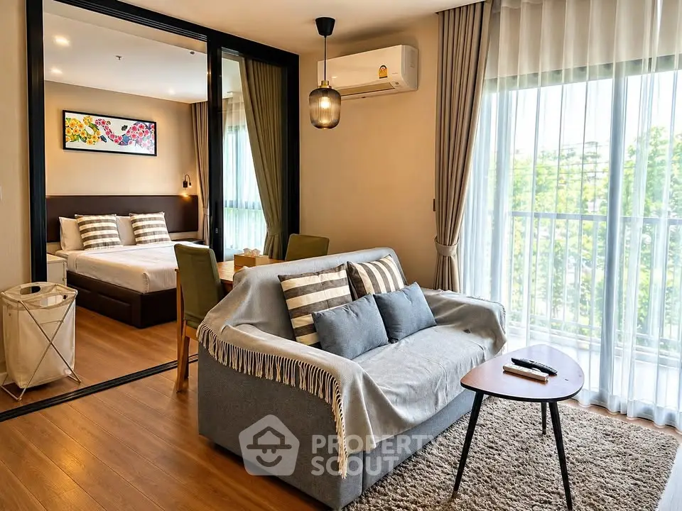 Modern living room with cozy sofa and view into stylish bedroom, featuring large windows and elegant decor.