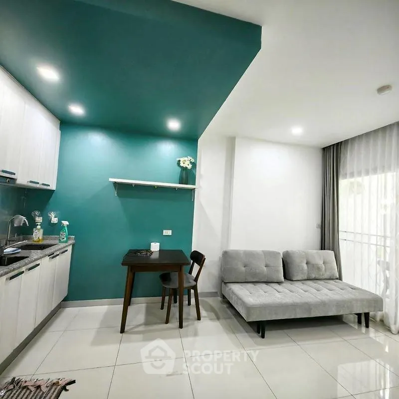 Modern open-layout kitchen and living room with teal accent wall and sleek furniture.