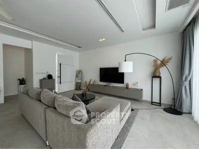 Modern living room with sleek gray sofa, flat-screen TV, and stylish decor in a bright, airy space.