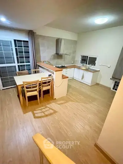 Modern kitchen with open layout and wooden flooring, featuring dining area and sleek cabinetry.
