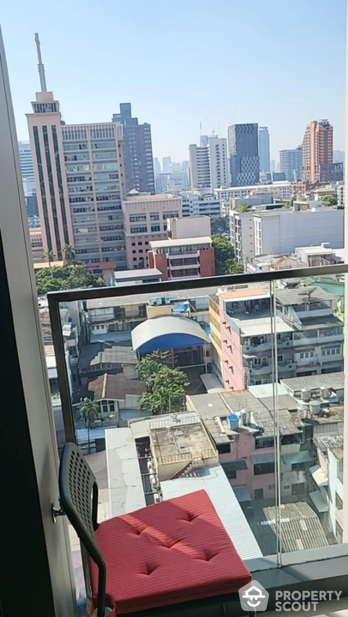 Stunning city view from modern balcony with glass railing and red cushioned chair.