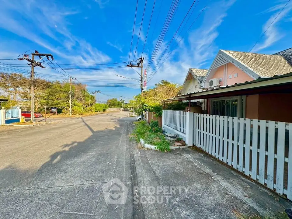 Charming suburban street view with cozy house and lush greenery under a clear blue sky.