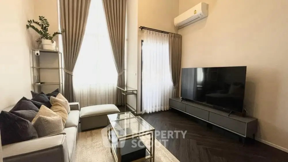 Modern living room with large TV, elegant curtains, and stylish furniture.