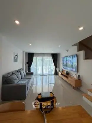 Spacious modern living room with sleek furniture and large TV, perfect for relaxation.