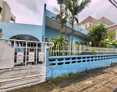 Charming blue house with lush greenery and white fence in a quiet neighborhood.