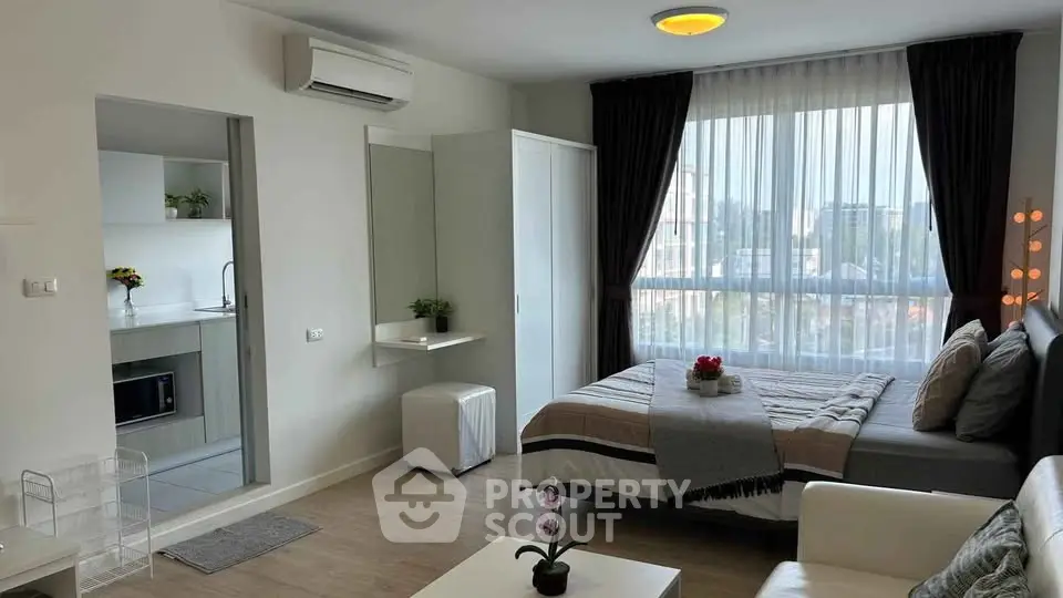 Modern studio apartment with cozy bedroom and kitchen area, featuring large window and stylish decor.