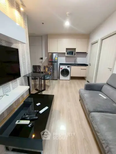 Modern living room with open kitchen, featuring sleek appliances and cozy seating area.