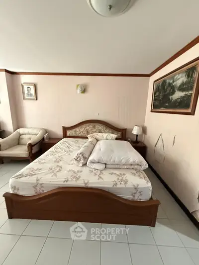 Cozy bedroom with elegant wooden bed frame and floral bedding, complemented by classic wall art and a comfortable armchair.