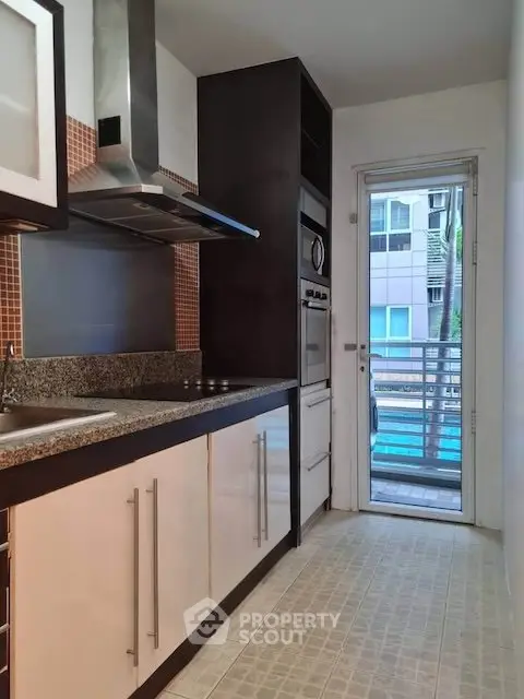 Modern kitchen with sleek cabinetry and stainless steel appliances, featuring a view of the balcony.