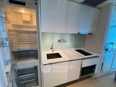 Modern kitchen with sleek white cabinets, built-in fridge, and electric cooktop in a compact layout.