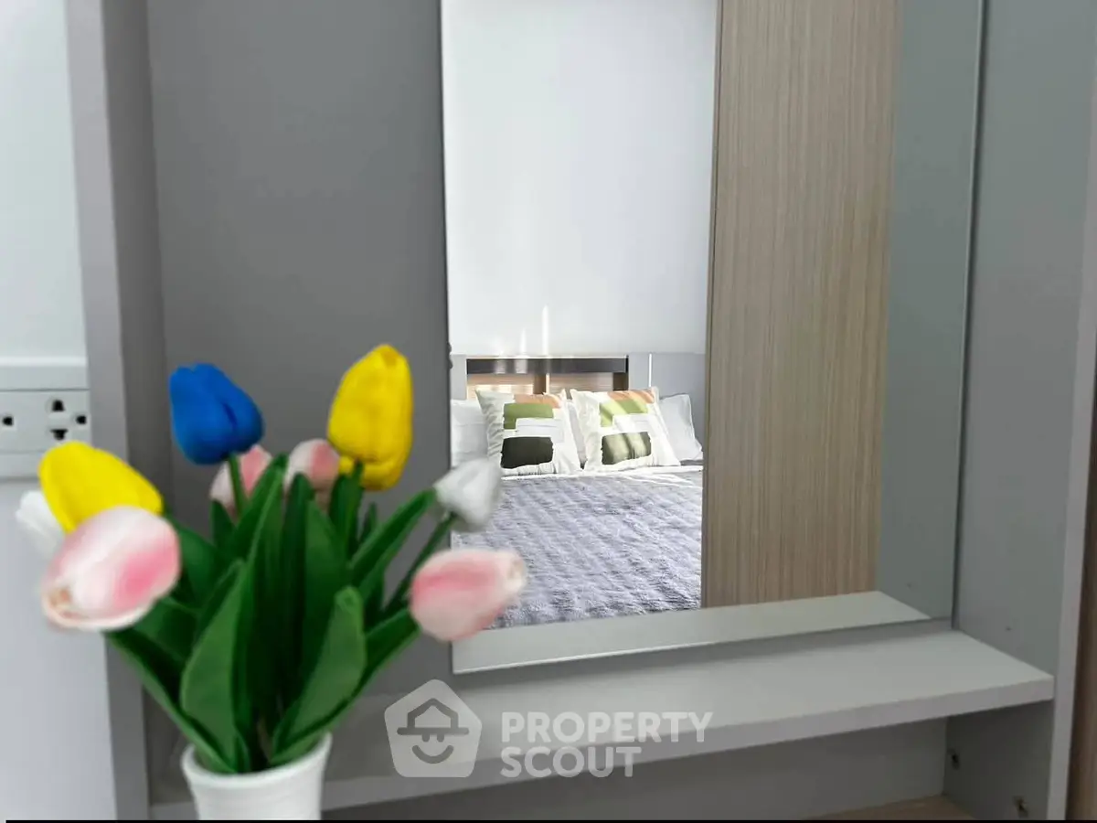 Stylish bedroom with modern decor and cozy bedding reflected in a mirror, featuring vibrant tulips in the foreground.